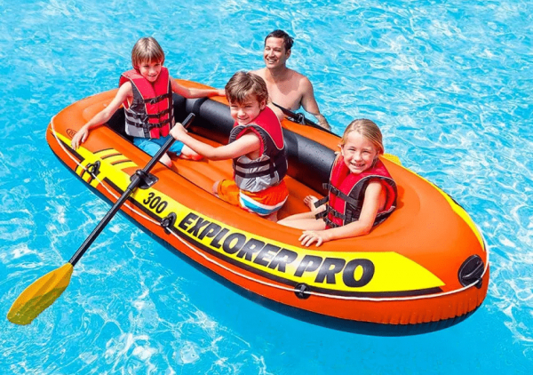 Tre barn sitter i båten medan en man står bredvid i poolen