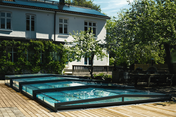 Pooltaket över en utomhuspool med träsarg och ett hus i bakgrunden