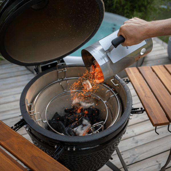 En hand häller kol från skorstenständaren ner i en grill