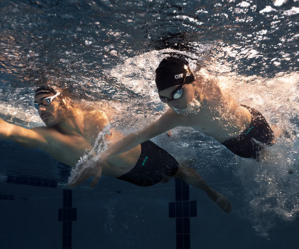 En man och en pojke i impulso badbyxor simmar under vatten