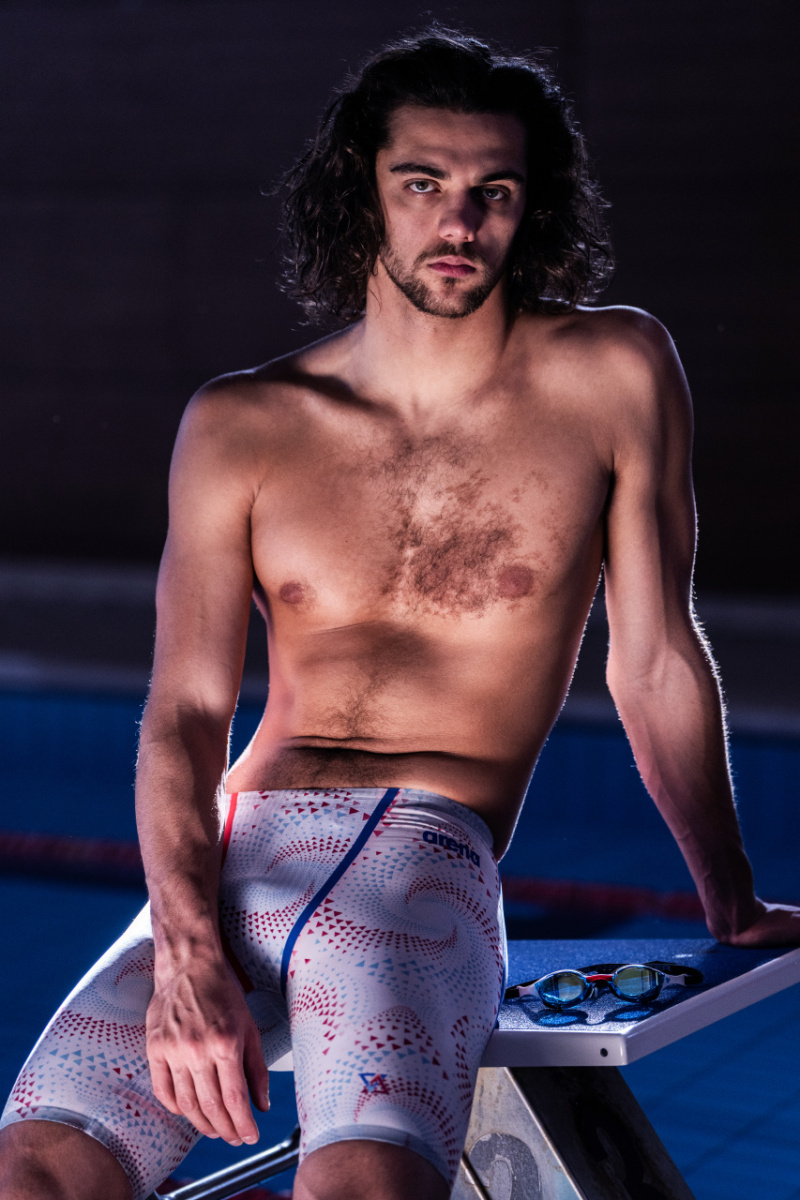 En man i badbyxorna sitter på en startplattform vid en pool