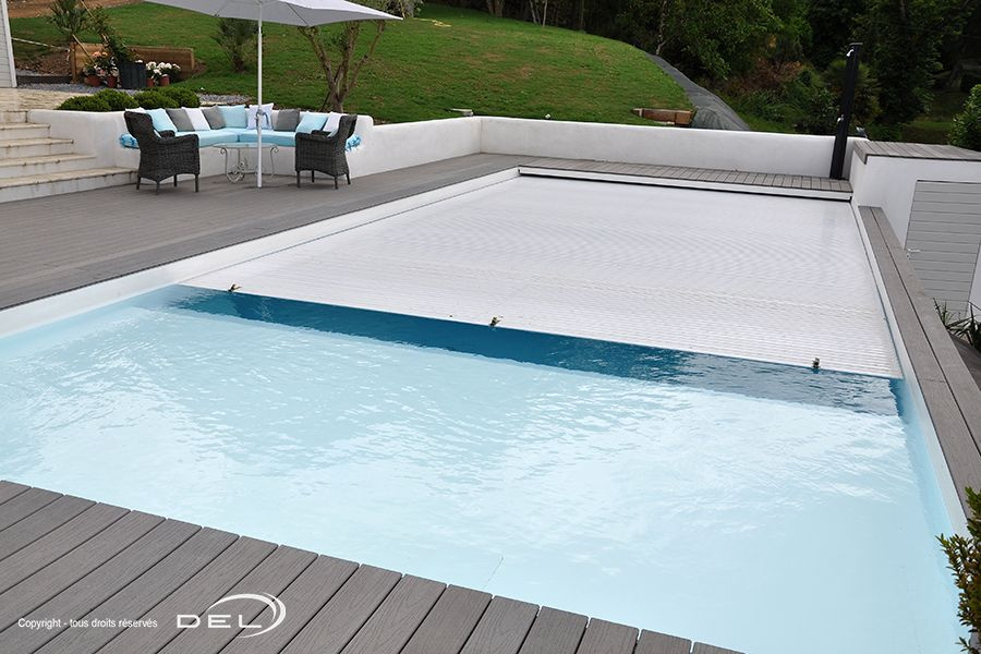 Rollenergy Lamelltäcke halvvägs öppnad i en pool med en trädgård i bakgrunden