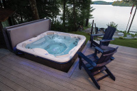 Spabad Signature Self-Cleaning 728 - Platinum Spabadet med ett öppet lock utomhus bredvid en med två loungestolar.