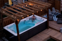 Swimspa 14AX AquaSport Ett öppet spabad bredvid en altan med en dam i vattnet