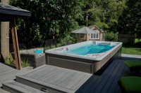 Swimspa 16EX Executive Trainer Swimspabadet inbyggt i en altan med en gräsmatta, ett lusthus och träd bakom