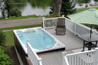 Swimspa 16EX Executive Trainer Swimspabadet inbyggt i en altan med gräs och vatten bakom