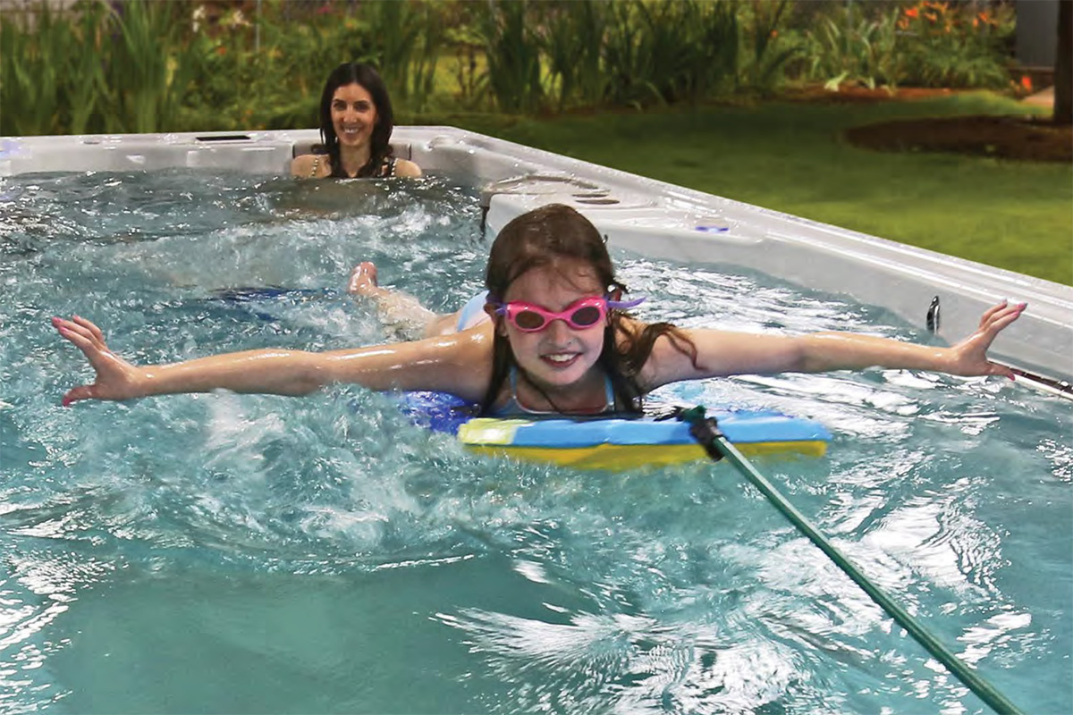 En tjej leker på en surfplatta i swimspabadet medan en dam sitter vid massagen i bakgrunden