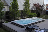 Swimspa 19DTAX AquaSport Swimspabadet på dagen på en uteplats med ett staket och växter i bakgrunden