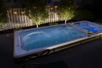 Swimspa 19DTAX AquaSport Swimspabadet på natten på en uteplats med ett staket och växter i bakgrunden