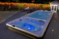 Swimspa 19DTAX AquaSport Swimspabadet på natten på en uteplats med ett staket och växter i bakgrunden