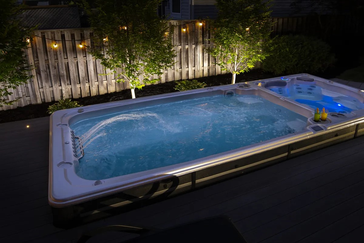 Swimspabadet på natten på en uteplats med ett staket och växter i bakgrunden