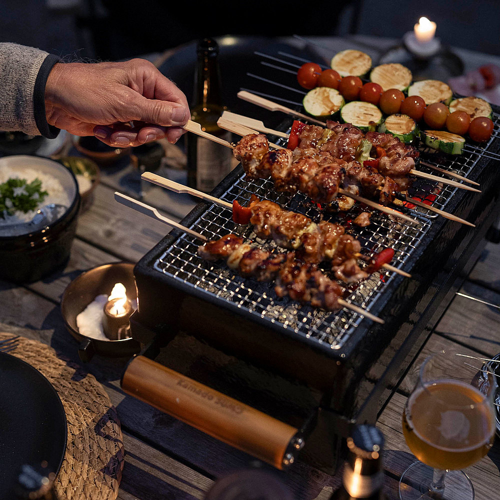 En hand vänder på spett med kött och grönsaker på grillen