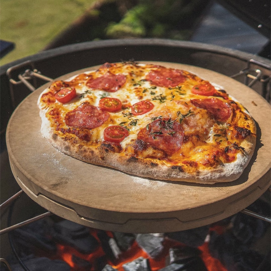 En pizzasten med en pizza på sig över en tänd grill