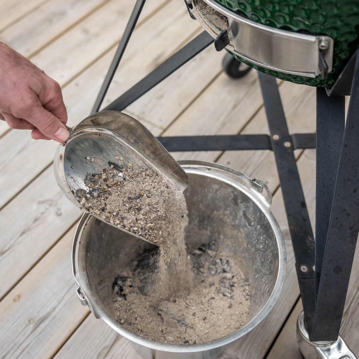 En hand häller aska från skopan ner i en hink