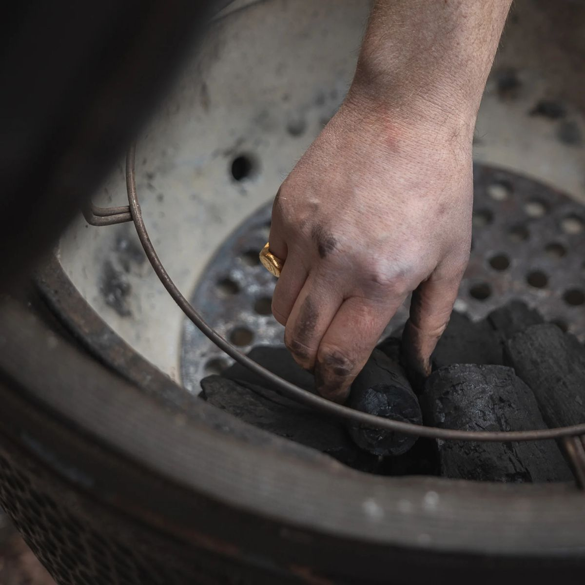 En hand lägger ner en kolbit i en grill