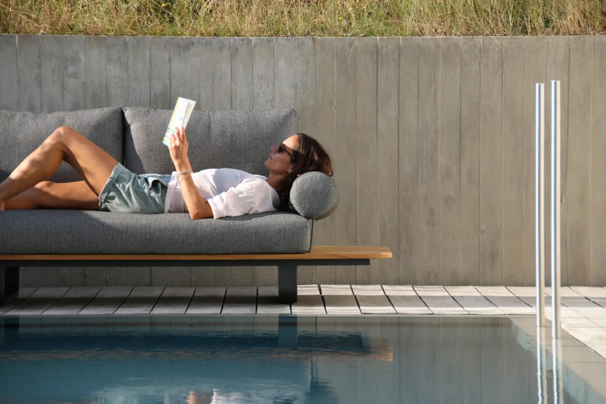 En kvinna läser på soffan vid en pool