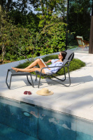En dam sitter i loungestolen med benen på pallen bredvid en pool