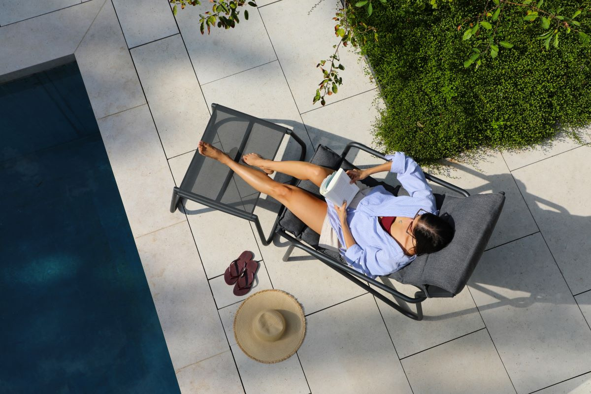 En dam sitter i loungestolen med benen på pallen bredvid en pool