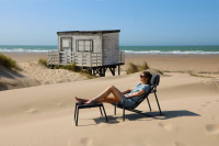 En dam sitter i loungestolen på en sandstrand framför havet