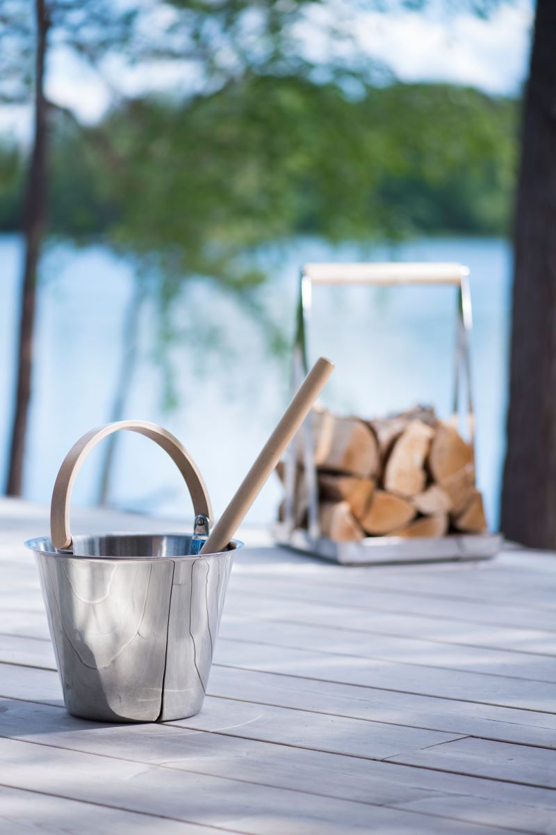 Den rostfria bastuhinken och skopan i förgrunden med vedkorgen i bakgrunden