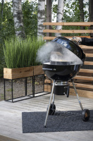 Kolgrill Gourmet 57 En hand lyfter locket av grillen som ryker