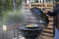 Går att använda med grytor, pizzastenar, och wokpannor En hand lyfter locket av grillen som ryker