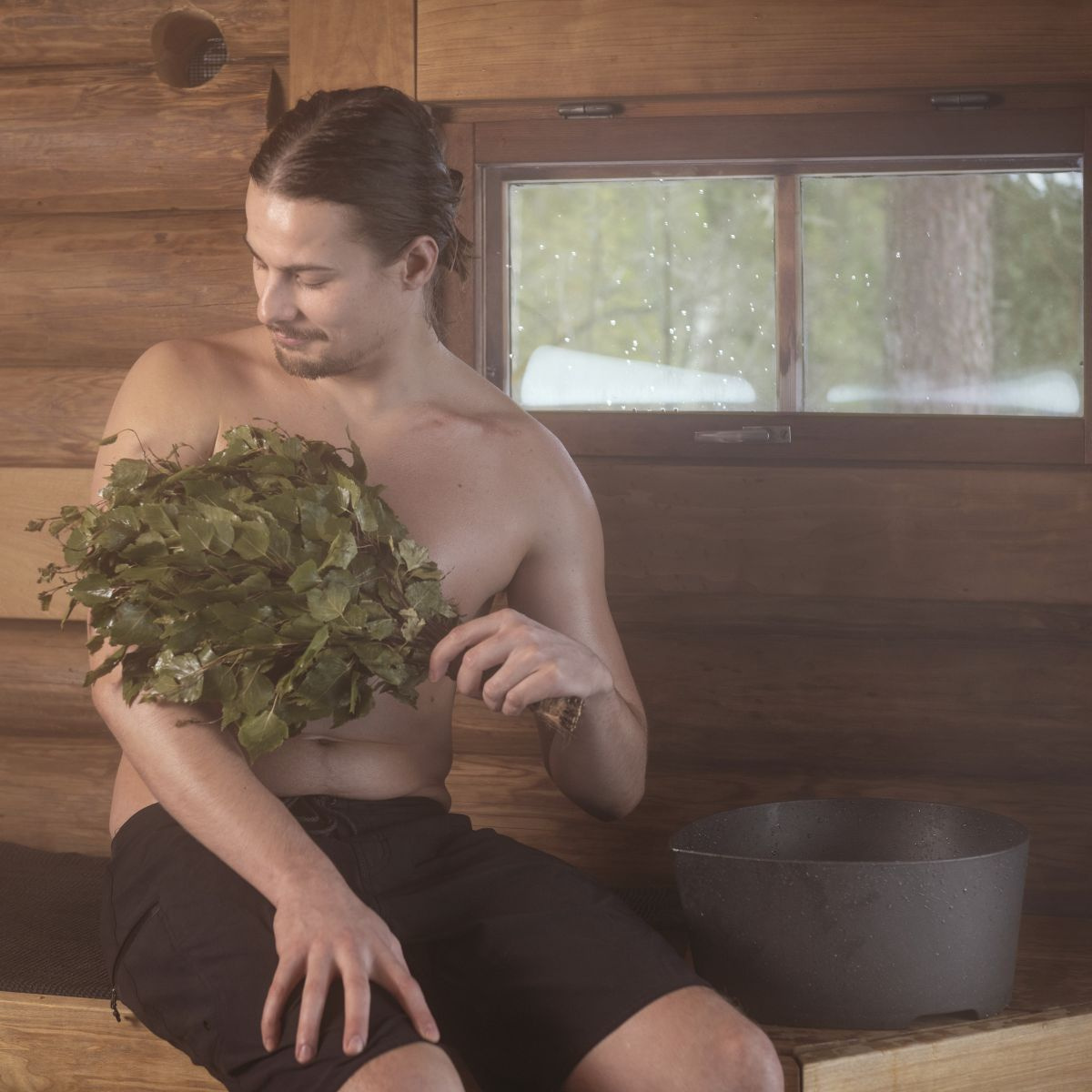 En man med en basturuska i handen har tvättfatet bredvid sig