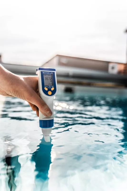 En hand håller testapparaten delvis nedsänkt i en pool